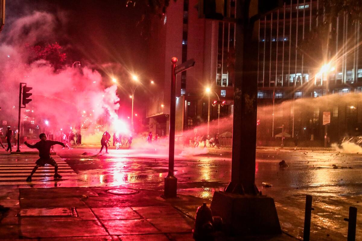 Manifestantes chocan con la Policía anoche en Lima. Miles de peruanos desafiaron ayer el toque de queda ordenado por el presidente Pedro Castillo para Lima y su vecina provincia de Callao y se manifestaron en la capital para pedir la renuncia del mandatario. EFE / VANGUARDIA