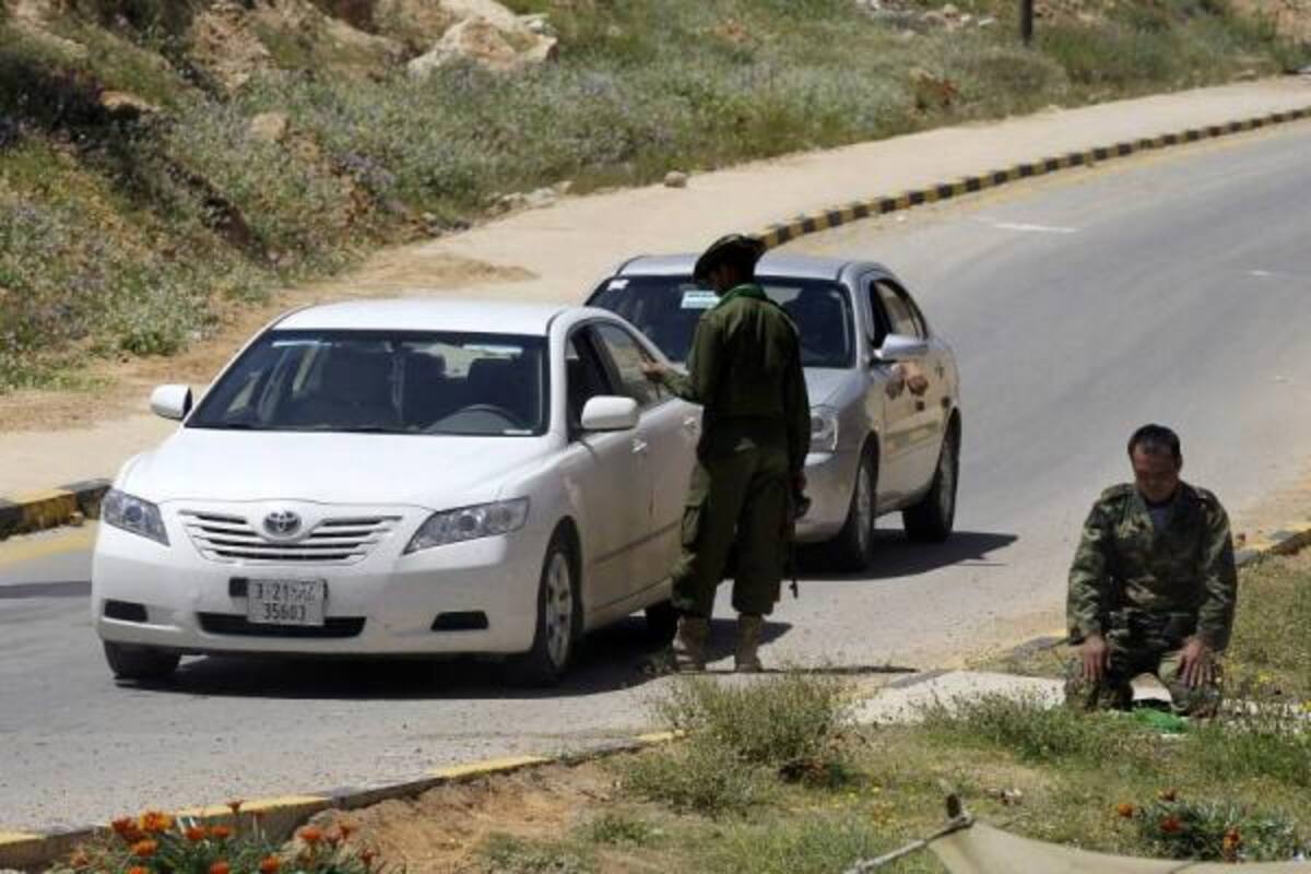 Un soldado libio de las fuerzas fieles al régimen de Gadafi inspecciona un auto mientras otro reza, en el punto de control de Gharyan, a unos 100 kms al suroeste de Trípoli.(Foto: EFE / VANGUARDIA LIBERAL)