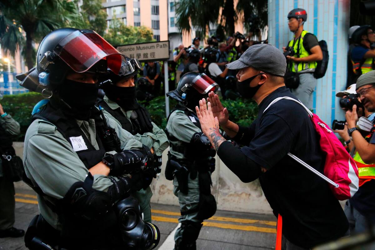 Un partidario de los manifestantes en favor de la democracia aún encerrados en la Universidad Politécnica habla con oficiales de la Policía antidisturbios que patrullan el campus en Tsim Sha Tsui, en Hong Kong. (Foto: EFE /VANGUARDIA)