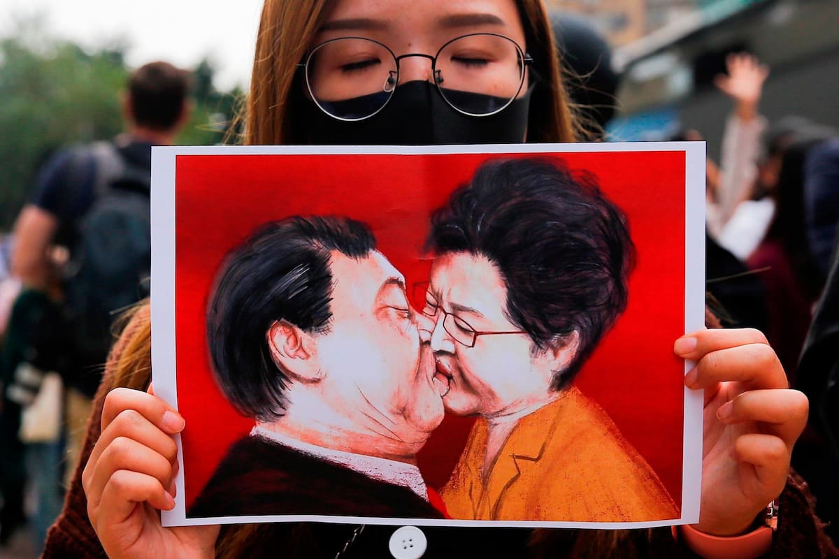 Una manifestante del movimiento prodemocrático de Hong Kong muestra una ilustración satírica que representa a la jefa del gobierno territorial, Carrie Lam, y al presidente chino, Xi Jinping, besándose, este martes, durante una protesta en Hong Kong (China). (Foto: EFE /VANGUARDIA)