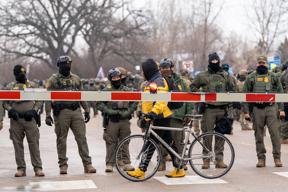Una persona pasa con una bicicleta frente a integrantes de la Policía que custodian la sede del Servicio de Inmigración y Control de Aduanas (ICE) este jueves, en Mineápolis (EE.UU.). Al menos ocho personas fueron detenidas durante el inicio de la segunda jornada de protestas por la muerte de una mujer estadounidense tras recibir varios disparos por parte de un agente del ICE, confirmaron testigos a EFE. EFE/ Angel Colmenares