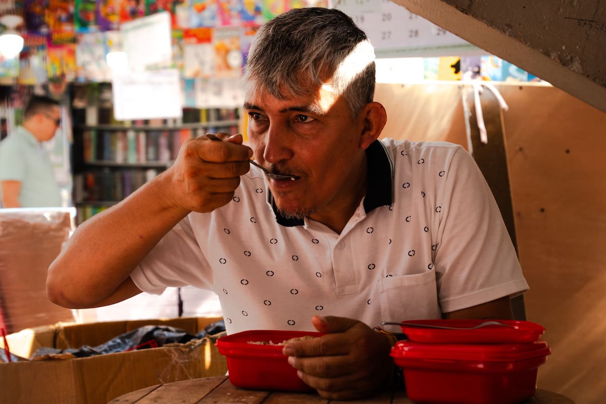 Julio César Pesca, vendedor ambulante, hace una pausa en su jornada para comer el único plato del día que lleva consigo en un portacomidas; una escena cotidiana en Bucaramanga, donde no todos pueden darse el lujo de las tres comidas diarias.