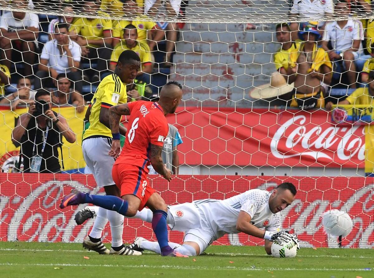 Colombia's goalkeeper David Ospina grabs a ball over the attack by Chile's midfielder Arturo Vidal (C) during their 2018 FIFA World Cup qualifiers football match in Barranquilla, Colombia, on November 10, 2016. / AFP / Luis Acosta
