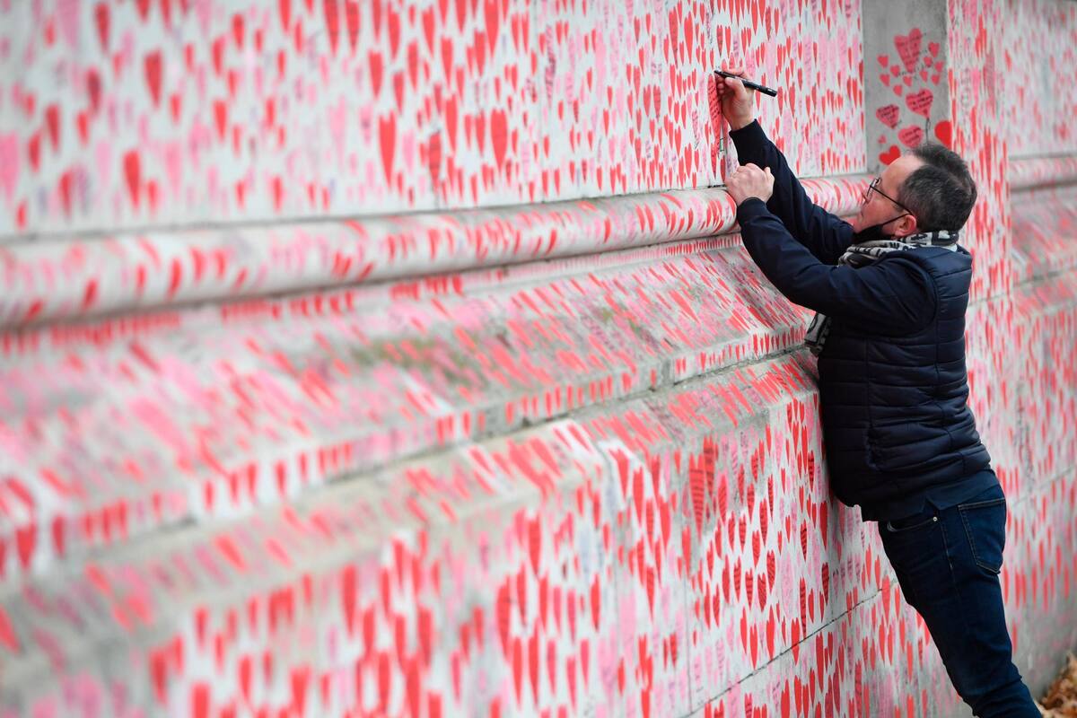 Un hombre escribe el nombre de una persona fallecida por el COVID-19 en un mural que honra a las víctimas de la pandemia en Londres. EFE / VANGUARDIA
