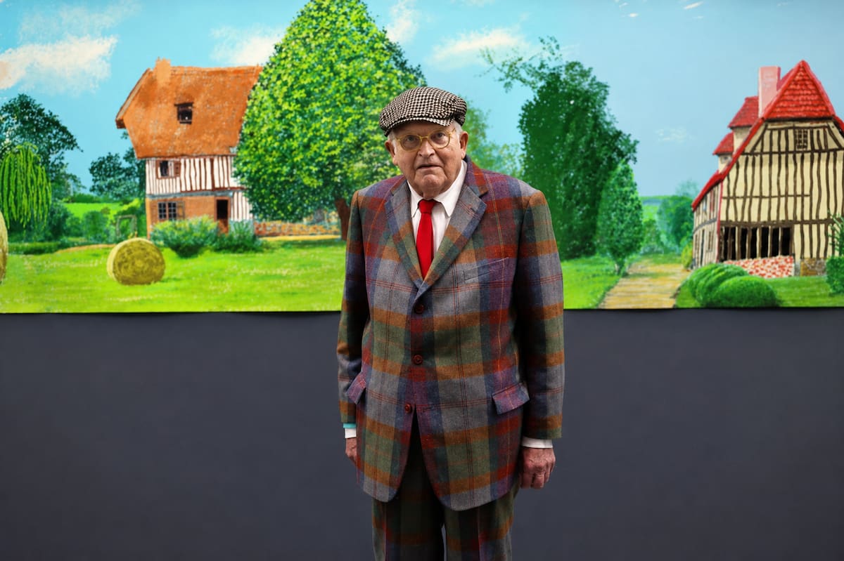 David Hockney posa frente a The Arrival of Spring in Woldgate, East Yorkshire in 2011, una obra inspirada en los paisajes de su natal Yorkshire y considerada una muestra de su constante renovación artística. Foto // gettyimages.