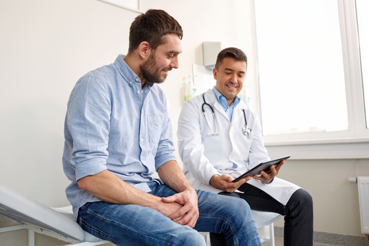 medicine, healthcare and people concept - smiling doctor with tablet pc computer and young man patient meeting at hospital