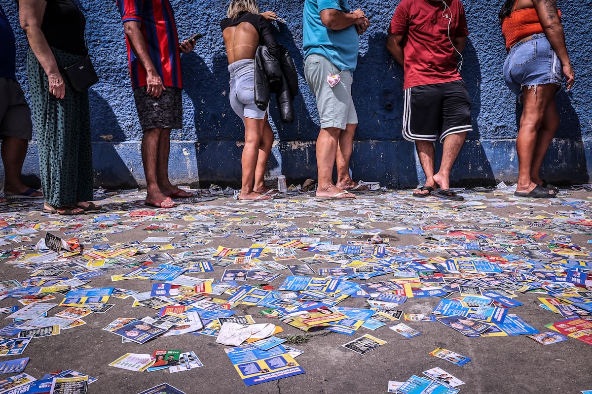 Personas esperan en un puesto de votación junto a publicidad electoral este domingo, en la escuela Bahia cerca al complejo de favelas de Maré, en Río de Janeiro (Brasil). EFE/ André Coelho