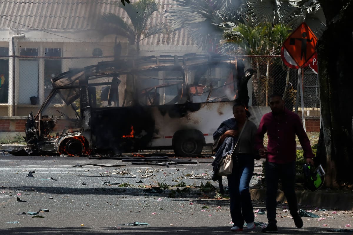Personas caminan frente a un vehículo afectado por una explosión este viernes, en inmediaciones del batallón de la Tercera Brigada del Ejército en Cali (Colombia). EFE/ Ernesto Guzman Jr