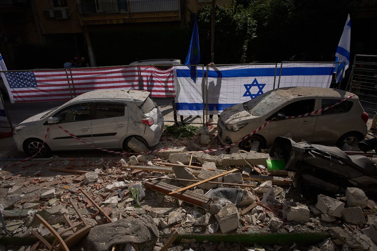 Las autoridades israelíes izan banderas de Israel y Estados Unidos en el lugar alcanzado por un misil iraní que causó la muerte de dos personas, en Ramat Gan, Israel. (Foto AP/Oded Balilty)
