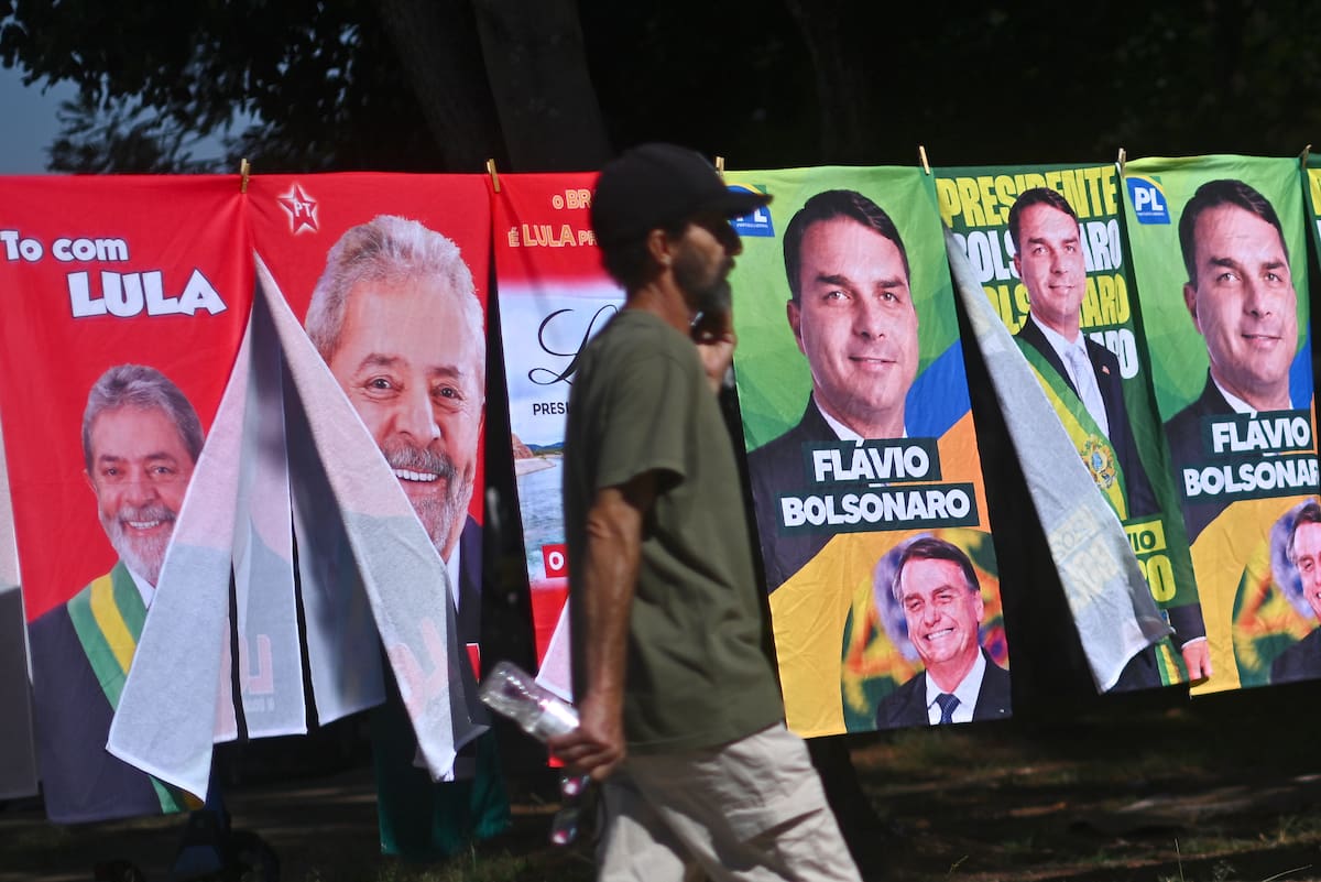 AME1288. BRASILIA (BRASIL), 30/09/2026.- Un hombre camina frente a una tienda informal de banderas con la imagen del presidente de Brasil y candidato a la reelección, Luiz Inácio Lula da Silva y del candidato presidencial, Flávio Bolsonaro, este lunes en Brasilia (Brasil). Mientras las encuestas hablan de una extrema igualdad entre el presidente progresista Luiz Inácio Lula da Silva y el ultraderechista Flávio Bolsonaro, analistas consideran que el resultado de las elecciones brasileñas del 4 de octubre depende de un amplio sector que observa el proceso con distancia y escepticismo: los indecisos. EFE/Andre Borges