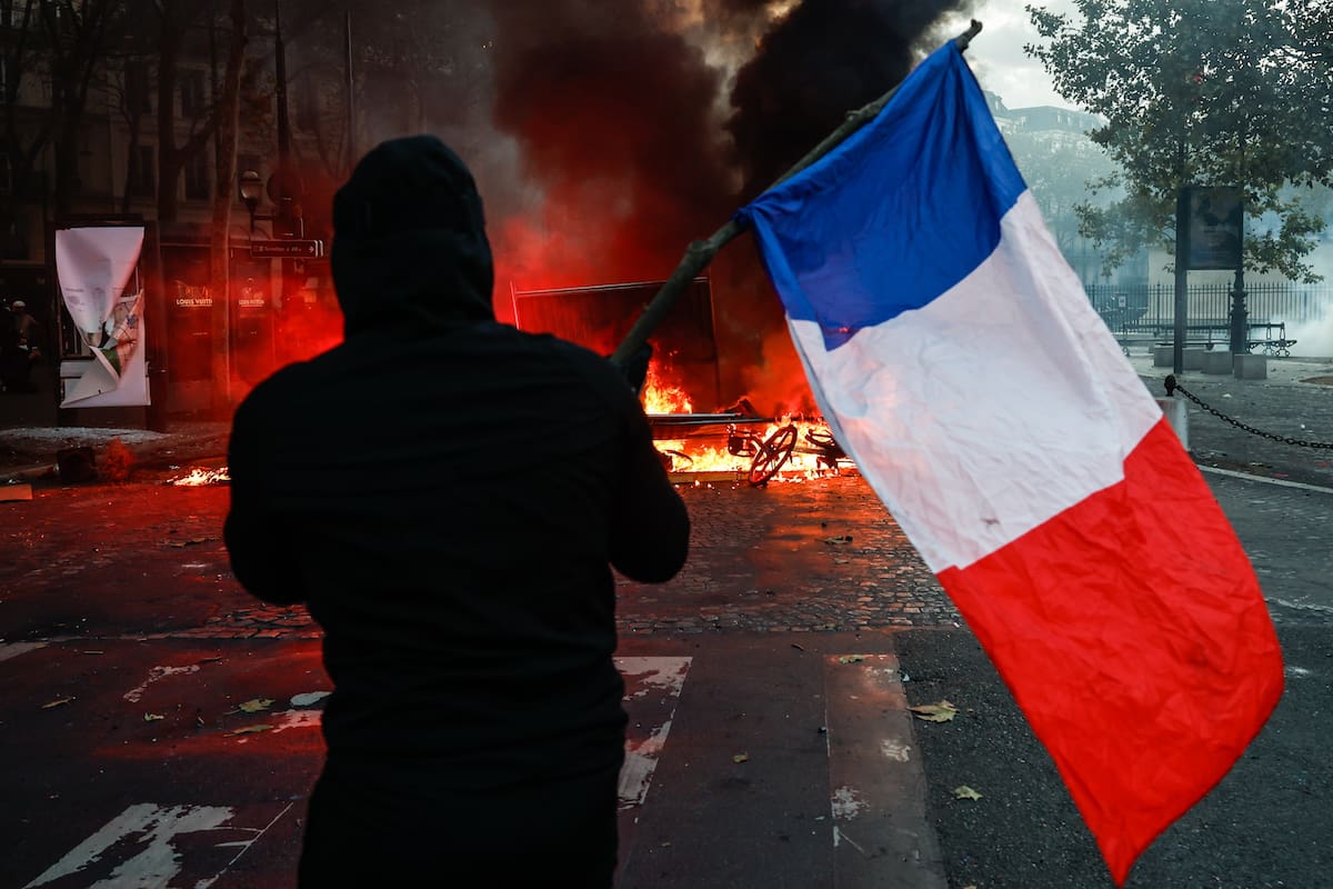 Paris (France), 17/10/2026.- A protester carrying a French flag faces police at Place de la Madeleine during a demonstration against rising living costs and cuts to public services in Paris, France, 17 October 2026. The nationwide mobilization brought together Yellow Vest (Gilets Jaunes) activists, high school and university students, trade unions and other groups protesting rising living costs, fuel prices and deteriorating public services, while demanding improvements in education and school conditions. (Protestas, Francia) EFE/EPA/MOHAMMED BADRA