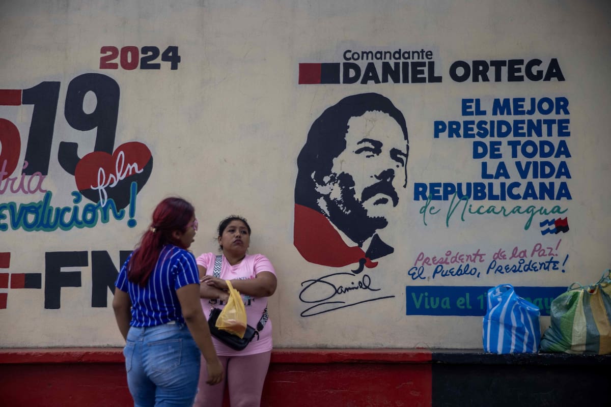 AME1375. SANDINO (NICARAGUA), 14/01/2025.- Dos mujeres conversan frente a un mural con la imagen del presidente de Nicaragua, Daniel Ortega, este martes en Sandino (Nicaragua). La Asamblea Nacional de Nicaragua comenzó a aprobar en segunda legislatura enmiendas a la Constitución Política, que transforma el Estado al denominarlo "revolucionario" y otorga un poder total al presidente del país, Daniel Ortega, y a su esposa y vicepresidenta, Rosario Murillo, sobre los demás poderes del Estado. EFE/ Str