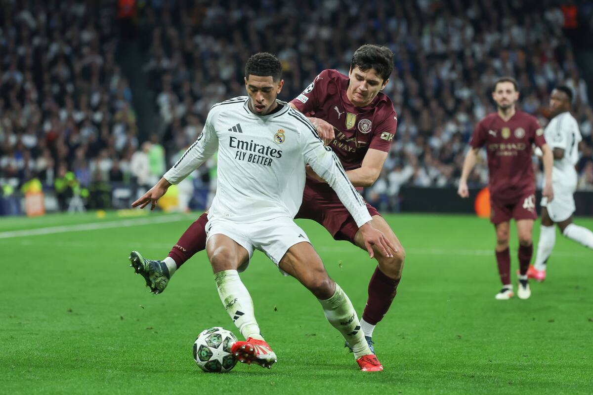 El centrocampista inglés del Real Madrid, Jude Bellingham, protege el balón ante el defensa uzbeko, Abduqodir Husanov, durante el encuentro correspondiente a los play off de la Liga de Campeones que disputan hoy miércoles Real Madrid y Manchester City en el estadio Santiago Bernabéu, en Madrid. (Foto: EFE / VANGUARDIA).