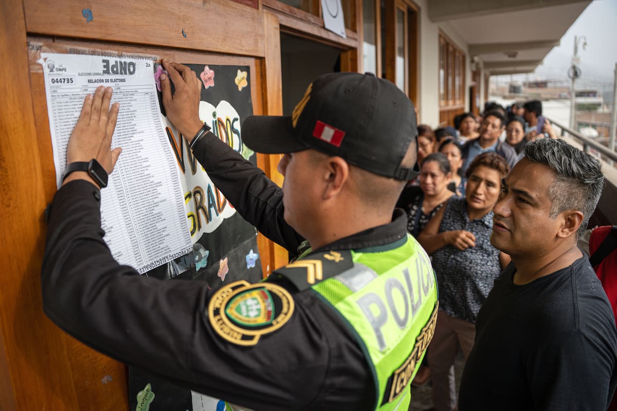 Un integrante de la Policía pega un cartel afuera de un aula de votaciones en el colegio Señor de los Milagros este lunes, en el distrito de Lurín (Perú). EFE/ John Reyes Mejia